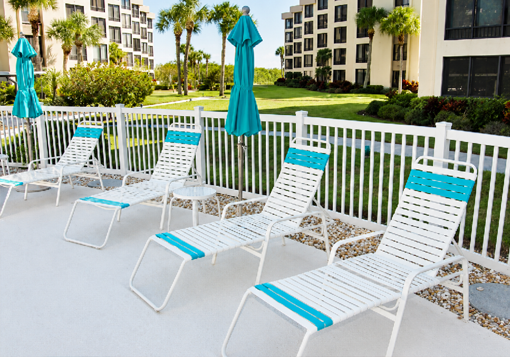 White commercial strap chaise lounges with turquoise accents arranged beside a resort swimming pool for stylish guest relaxation.